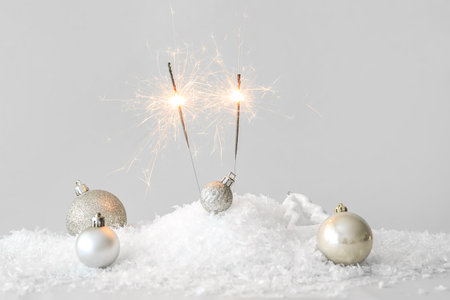 Burning Christmas sparklers in heap of snow and decorations on table against white backgroundの写真素材