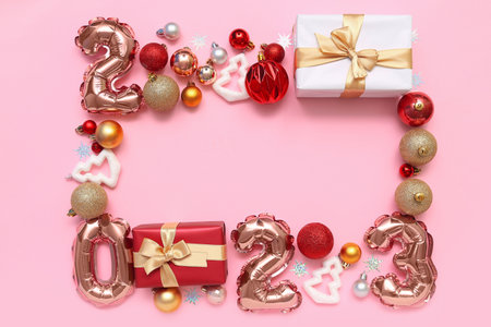 Frame made of figure 2023 with balloons, gifts and Christmas decor on pink background