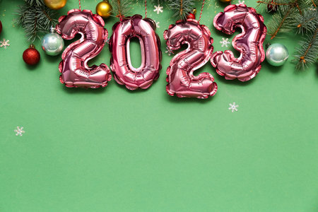 Figure 2023 made of foil balloons with Christmas branches and balls on green background