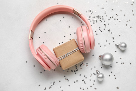 Modern headphones with Christmas gift, balls and sequins on light backgroundの写真素材