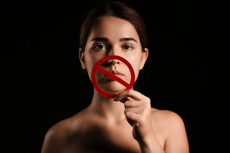 Young woman with prohibition sign on dark background. Censorship concept