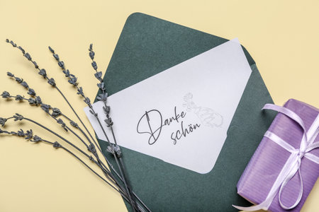 Card with text DANKE SCHON, envelope, gift box and lavender flowers on beige backgroundの写真素材