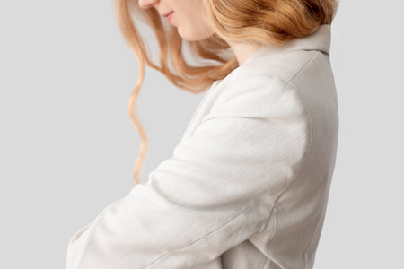 Young blonde woman with curly hair in stylish jacket on light background, closeup