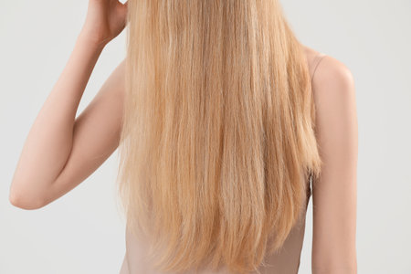 Blonde woman touching long hair on light background, closeupの写真素材