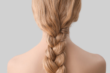 Young woman with pigtail hairstyle on light background
