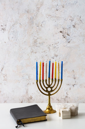 Menorah with Torah and gifts for Hanukkah on table near light wallの写真素材