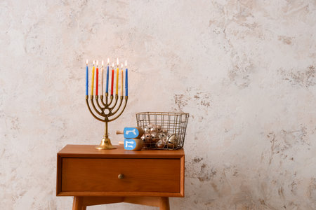 Basket with bells, dreidels and menorah for Hanukkah on table near light wallの写真素材