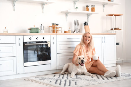 Mature woman with cup of coffee and cute Labrador dog in kitchenの写真素材