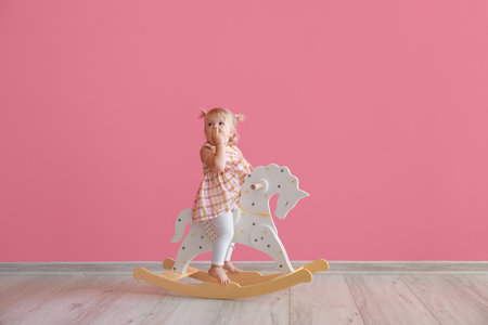 Adorable baby girl with rocking horse near pink wallの写真素材