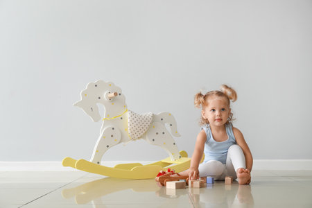 Adorable baby girl with rocking horse and toys near light wallの写真素材