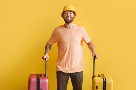 Handsome young man with suitcases on yellow backgroundの写真素材