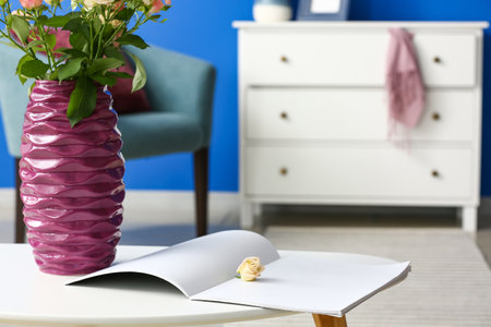 Purple vase with beautiful roses and open magazine on table in roomの写真素材
