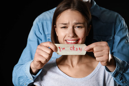 Man covering mouth of scared young woman on dark background. Violence concept