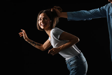 Man pulling hair of scared woman on dark background. Violence concept