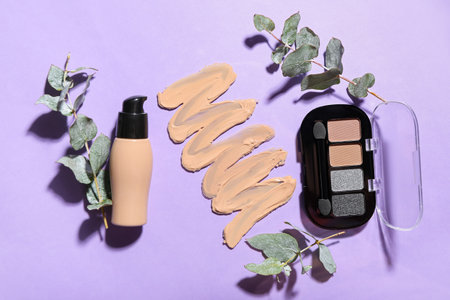 Smear of makeup foundation, eyeshadows and eucalyptus branches on purple backgroundの写真素材