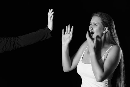 Man beating scared woman on dark background. Violence concept