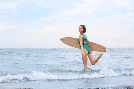 Beautiful young woman with surfboard on beach at resort