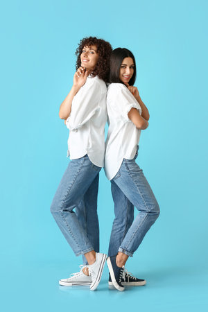 Young smiling sisters standing back to back on color background