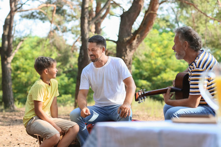 Senior man playing guitar for his son and little grandson in forestの写真素材