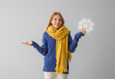 Young redhead woman in warm scarf with big snowflake on gray backgroundの写真素材