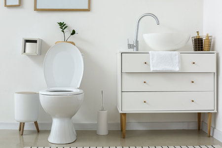 White toilet bowl and chest of drawers near light wall in restroomの写真素材