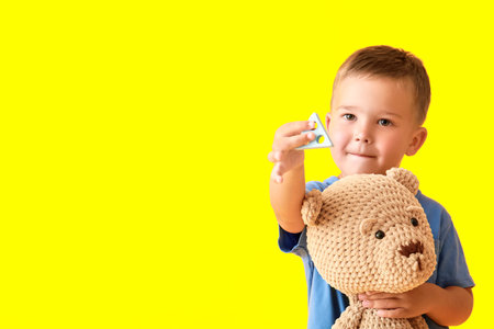 Cute little boy with building block and teddy bear on yellow backgroundの写真素材