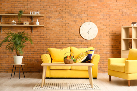 Interior of living room with sofa, armchair and table with fruit basket near brick wallの写真素材