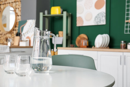 Jug with water and empty glasses on dining table in modern kitchenの写真素材
