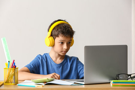Little boy doing homework online at table on light backgroundの写真素材