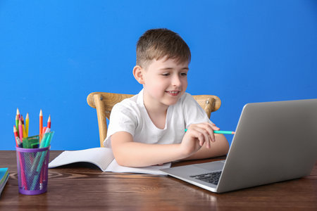 Little boy doing homework online on color background