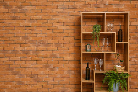 Shelving unit with bottles of wine, glasses and houseplants near brick wallの写真素材