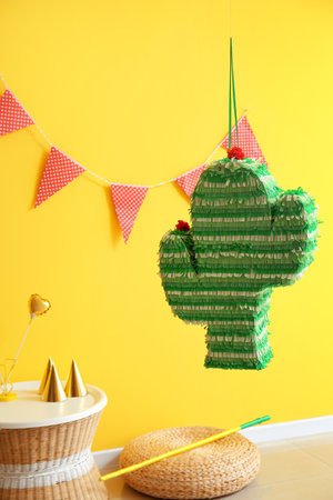 Mexican pinata in shape of cactus hanging near yellow wall