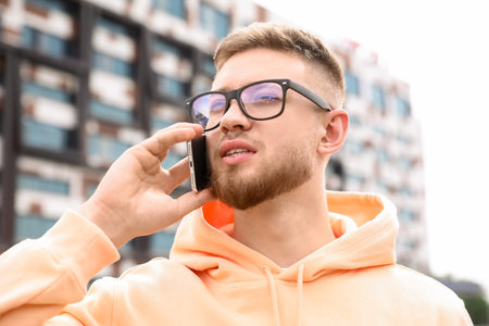 Young guy in stylish hoodie talking by phone outdoorsの写真素材