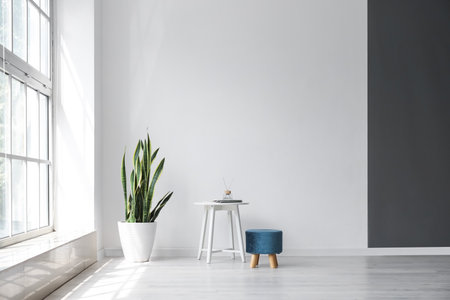 Interior of light room with table, pouf and houseplant