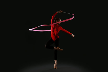 Beautiful young woman doing gymnastics with ribbon on black backgroundの写真素材
