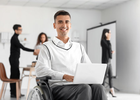 Man in wheelchair with laptop in officeの写真素材