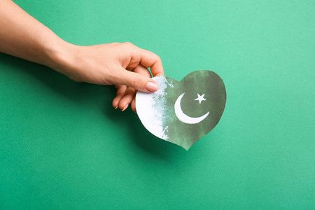 Female hand with flag of Pakistan in shape of heart on color backgroundの写真素材
