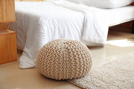 Pouf on floor near bed in light roomの写真素材