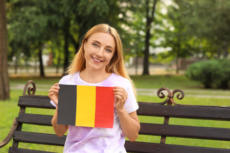 Mature woman with flag of Belgium sitting on bench in parkの写真素材