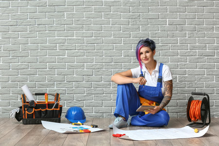 Female electrician with tools near brick wallの写真素材
