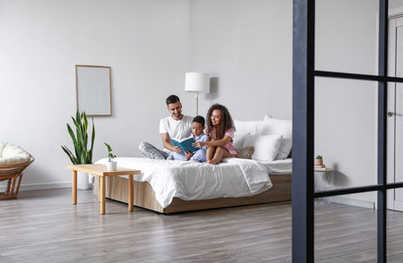 Happy interracial family reading book in bedの写真素材