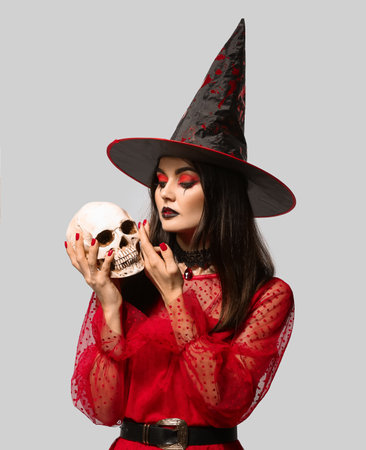 Young witch with skull on light background