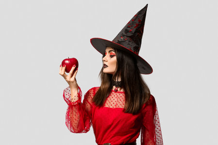 Young witch with apple on light background