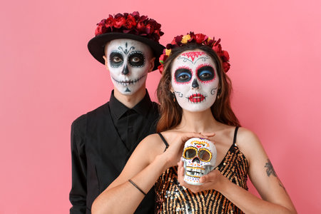 Young couple with painted skull on faces against color background. Celebration of Mexico's Day of the Dead (El Dia de Muertos)の写真素材