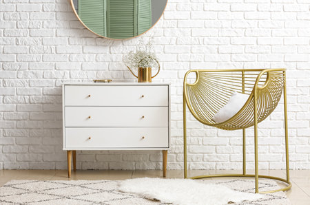 Stylish armchair with chest of drawers and mirror in interior of roomの写真素材