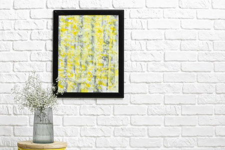 Vase with beautiful gypsophila flowers on table near white brick wall with picture in room