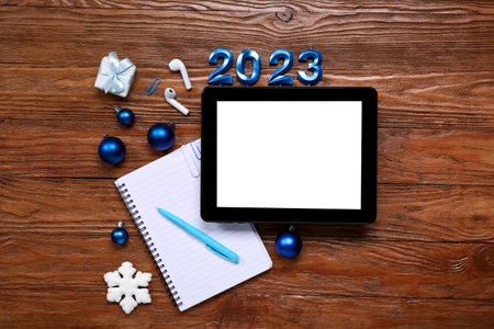 Tablet computer with notebook, earphones and Christmas decor on wooden background