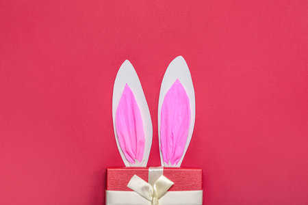 Paper bunny ears with Christmas gift on red backgroundの写真素材