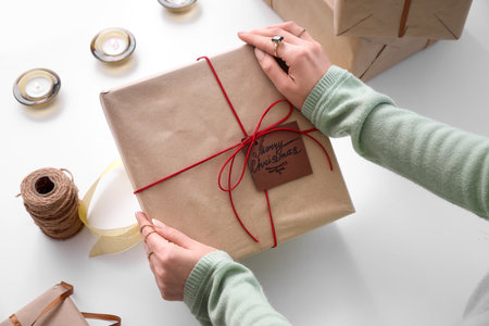 Woman with beautiful Christmas gift box on white table, closeup