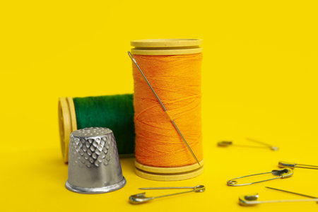 Thread spools, needle, thimble and safety pins on yellow background